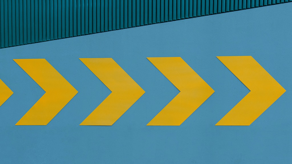 Yellow arrows pointing right on blue building Clark Van Der Beken on unsplash
